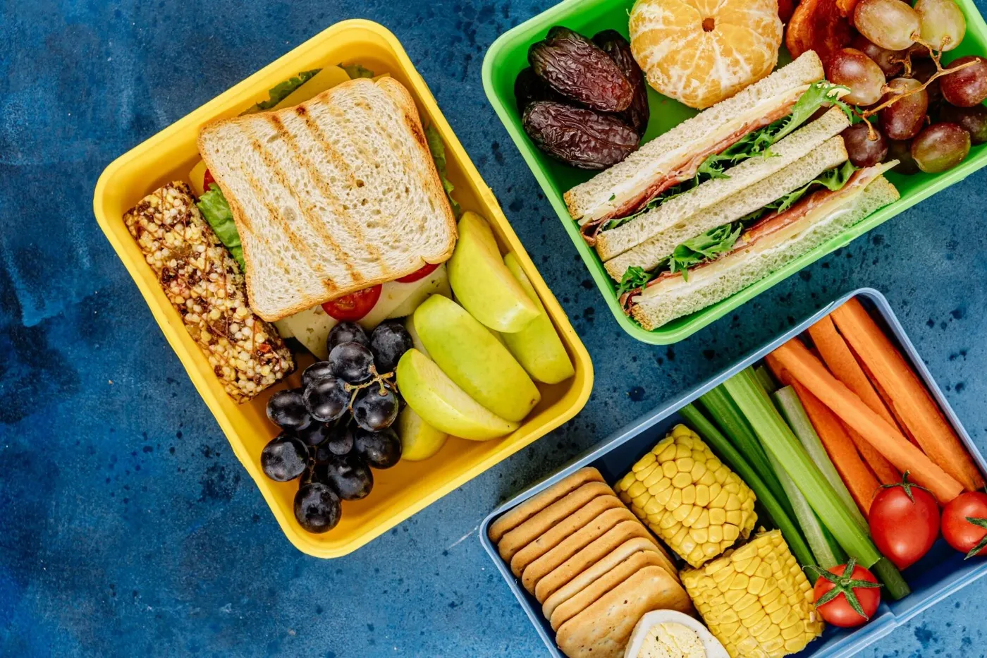 Lunchboxes with sandwiches, apple slices, grapes, carrots, celery and corn